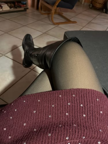 Cliente portant le collant polaire effet transparent avec une jupe et des bottes noires.