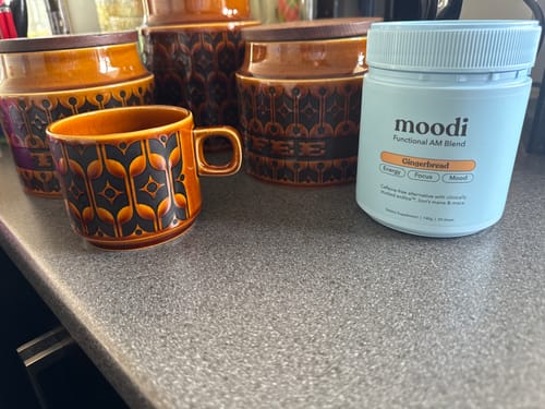 Customer shows their moodi Gingerbread blend on a counter next to a patterned mug and canisters.
