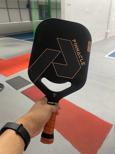 Reviewer holding the black and gold Toby's Pro Pinnacle Edgeless Pickleball Paddle on an indoor court.