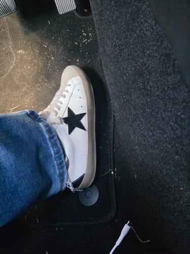 Customer's white sneaker with a large black star on the side, shown on their foot in a car.