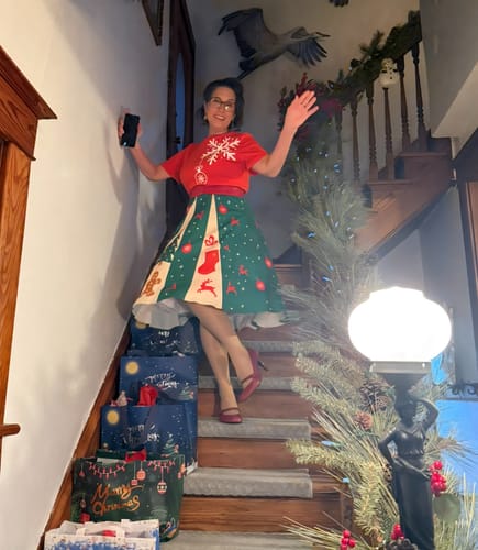 Reviewer posing on a staircase in the Red & Green 1950s Christmas Snowflake Swing Dress, showing off its full skirt.