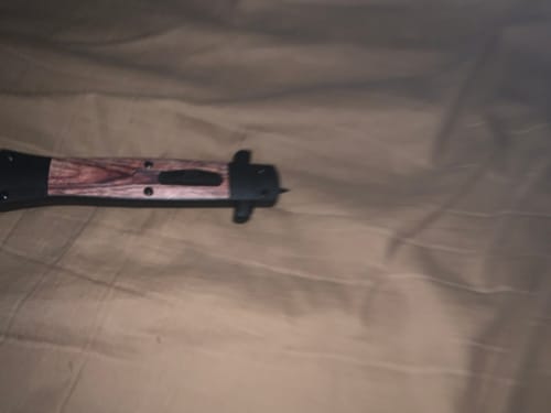 A reviewer's close-up of the Culprit OTF Stiletto knife, showing the dark wood-look handle in its closed state.