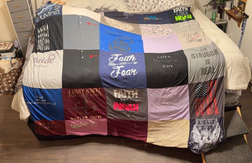 Customer's large, custom T-Shirt Quilt made of many colorful shirts spread across a bed in a bedroom.