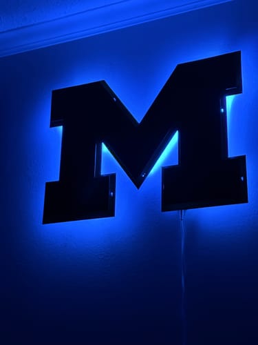 Reviewer's Michigan Wolverines 'Block M' wall art mounted on a wall and illuminated with blue LED backlighting.