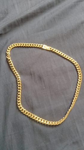 Cliente mostrando su cadena Cuban Link Oro sobre una superficie de tela oscura y arrugada.