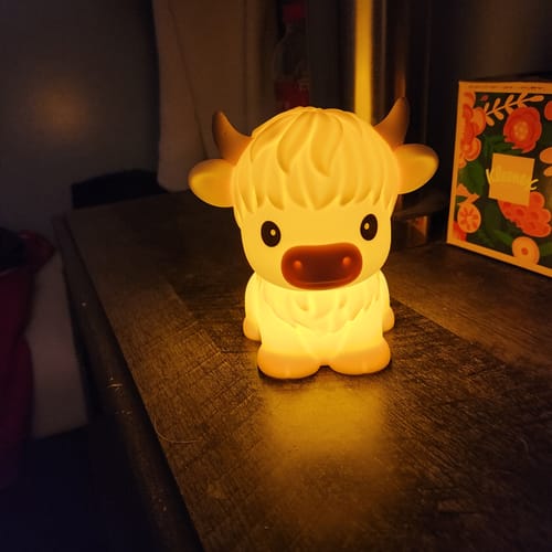 Customer's Highland Cow LED Night Light glowing with warm light on a wooden nightstand.