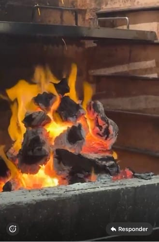 Cliente con carbón encendido en una parrilla, listo para cocinar el Rib Eye Steak.