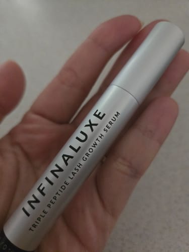 Customer holding the silver tube of Infinaluxe Triple Peptide Lash Growth Serum.