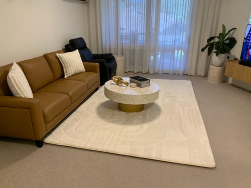 Reviewer's large, cream Mellow Mat in their living room with a tan sofa and coffee table.