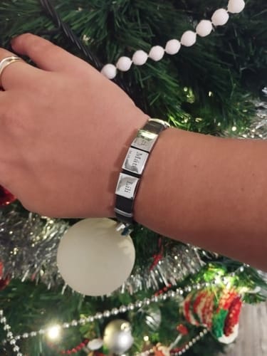 Reviewer wearing the personalized Lux bracelet with several engraved pendants on their wrist in front of a Christmas tree.