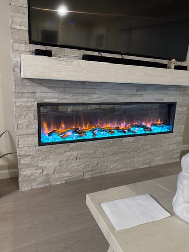 Customer's Dynasty Harmony electric fireplace installed in a stone wall, showing orange flames above a bright blue fire bed.
