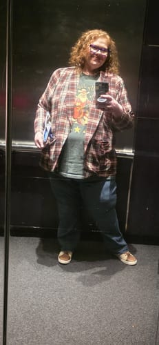 Reviewer wearing the Giddy Up Jingle Horse Tee with a plaid blazer and jeans, taking a mirror selfie.
