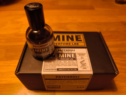 Cliente mostra la boccetta di profumo PATCHOULI e la sua scatola nera su un tavolo.