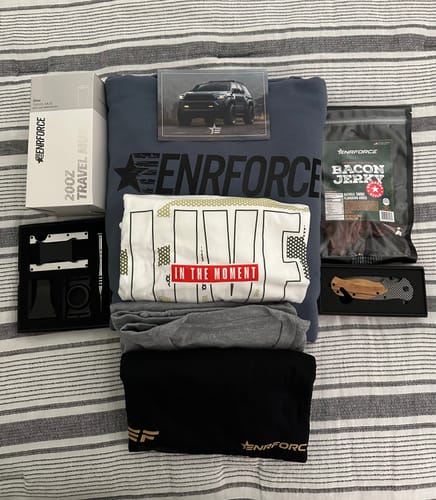 Customer's items from the ENR#70 Exclusive Mystery Box, including a hoodie, tees, jerky and accessories, laid out on a bed.