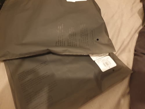 Recensent toont de twee grijze verpakkingen van de Fear of God Essentials set op een bed.