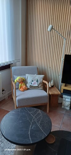 Klant toont de beige Wise Fauteuil met eikenhouten frame in een sfeervolle woonkamer.