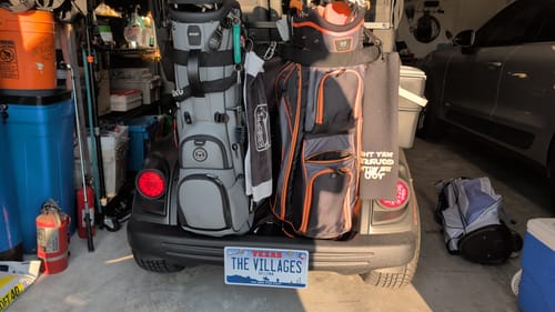 Customer's custom Texas Metal License Plate with 'THE VILLAGES' text, mounted on the back of a golf cart in a garage.