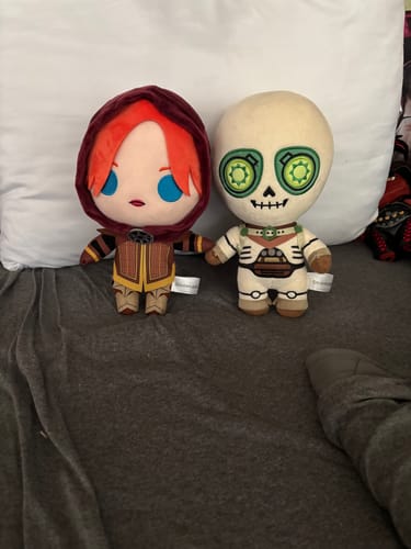 Reviewer's Leliana Collector's Plush sitting on a bed and holding hands with another plush character.