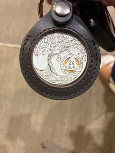 Customer holding the white 24 Hours Sobriety Medallion in a grey leather keychain holder.