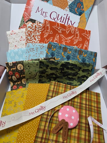 Customer's Mrs Quilty Subscription Box, open and displaying colorful, patterned fabrics, a booklet, and sewing notions.
