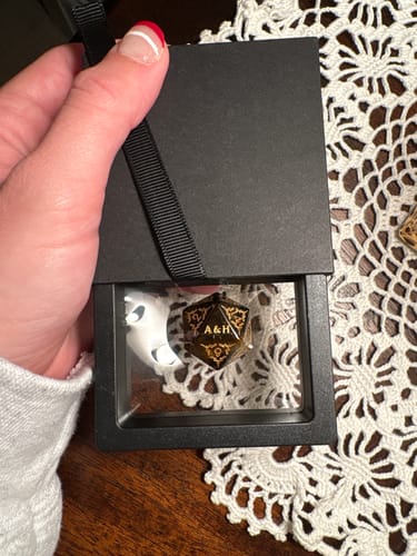 Reviewer holding a black display box showing a personalized D20 dice with the gold initials 'A&H'.