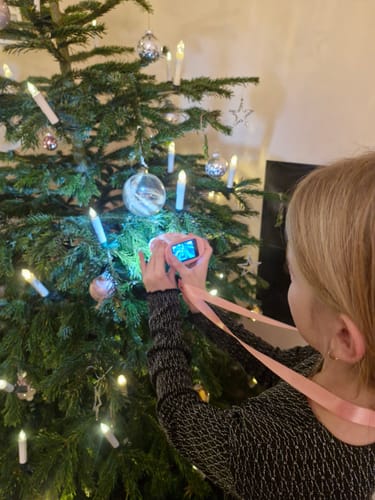 Ein Kunde zeigt ein Kind, das mit dem rosa Abenteuer-Mikroskop einen geschmückten Weihnachtsbaum untersucht.