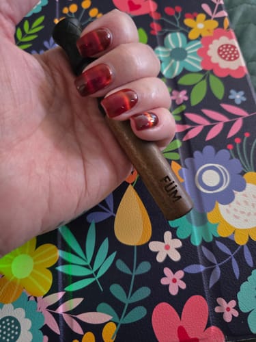 Customer's hand holding a wooden FÜM device against a colorful floral background.
