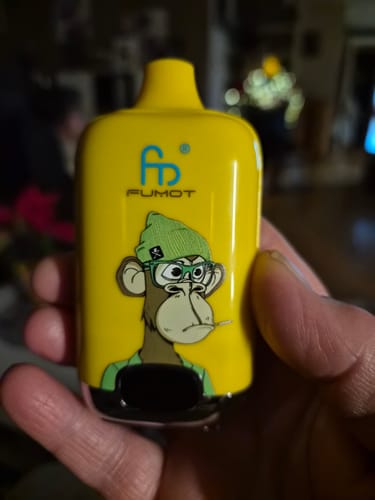 Ein Kunde hält die gelbe RANDM Digital Box 12000 Vape mit einem Cartoon-Affen-Aufdruck in der Hand.