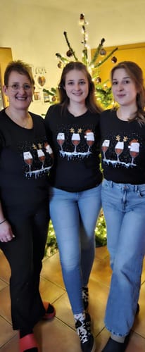 Drei Kundinnen tragen das passende schwarze Weihnachtswein Premium Organic Shirt vor einem Weihnachtsbaum.