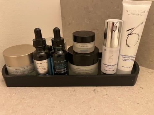 Reviewer's SkinCeuticals AGE Advanced Eye cream in a black tray with other skincare products on a counter.