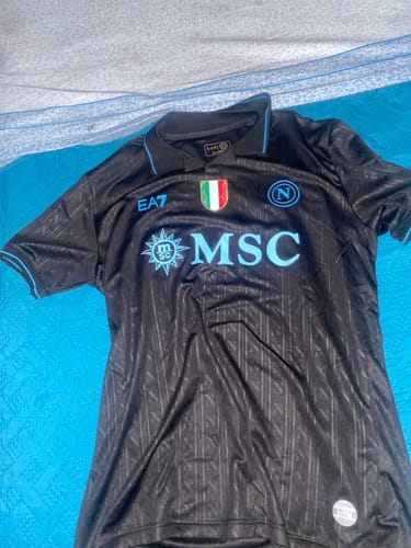 Recensore mostra la Maglia Napoli Third, di colore nero con dettagli azzurri, stesa su un letto.