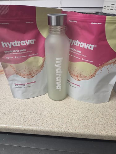 Reviewer's two pink pouches of hydrava electrolyte salts in Strawberry Lemonade flavor next to a branded water bottle.