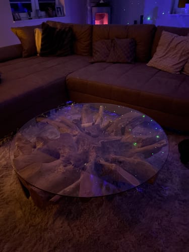 Kunde zeigt den Wurzel Couchtisch NAGA in einem stimmungsvoll beleuchteten Wohnzimmer.