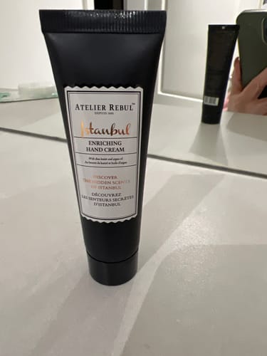Recensent toont de zwarte tube Istanbul Handcrème staand op een witte ondergrond.