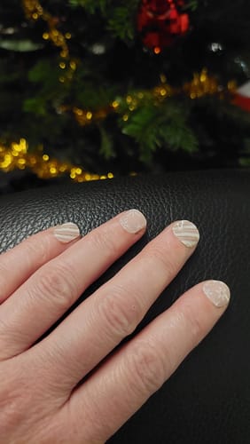 Hand einer Kundin, die die ‚Blush Wonderland‘ UV-Gel-Folien trägt, die ein zartes Design aus Streifen und Schneeflocken zeigen.