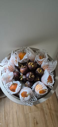 Ein Kunde zeigt die erhaltenen Granadillas in weißen Netzen und die Mangostans in einer Schale.