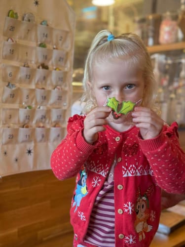 Customer's child holding a festive holly-shaped biscuit with the fabric advent calendar in the background.