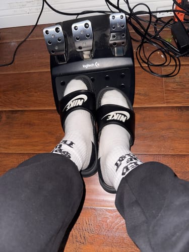 Reviewer wearing the white SPEED CREW SOCKS with black slides in front of a set of gaming pedals.
