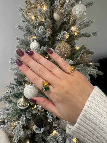 Customer's hand wearing the Navae Birthstone Ring with a vibrant green and a yellow stone in a festive setting.
