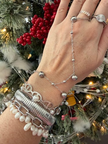 Customer's hand showing the silver-colored Netra Bangle styled with a stack of other bracelets and rings.
