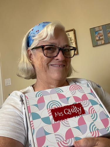 Reviewer smiling while holding the colorful box for the Mrs. Quilty Plushies pattern bundle.