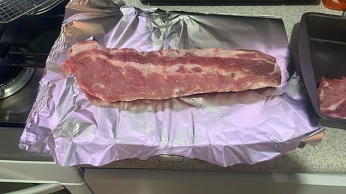 Reseñador mostrando un costillar de Baby Back Ribs de Cerdo crudo sobre papel de aluminio.