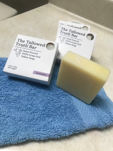 Reviewer's unwrapped Tallowed Truth Bar on a blue towel, with two product boxes in the background.