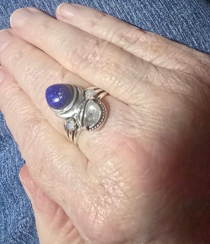 Customer's hand wearing the large Lapis and Moonstone Saturn Celestial ring on their middle finger.