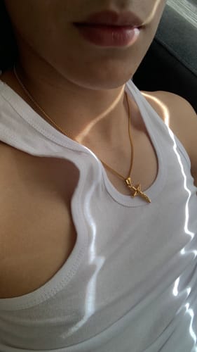 Primer plano de un cliente usando el colgante Cross Minimal Oro con una camiseta blanca sin mangas.