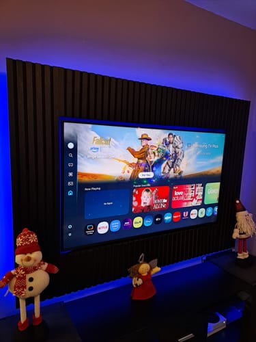 Customer's dark Acoustic Slatted Wall Panels installed as a feature wall behind a TV, backlit with blue light.