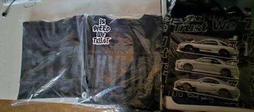 Customer's new TOKYO TRIBUNE TEE folded in its clear packaging, next to the included car stickers.