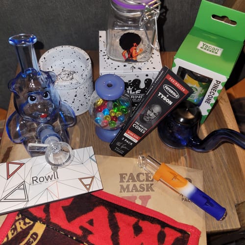 Customer's items from the Mystery Box, including a blue bear-shaped bong, a grinder, and other smoking accessories on a table.