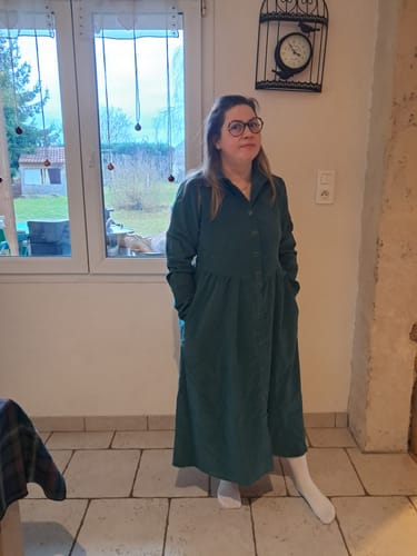 Cliente portant la Robe Arlène vert émeraude. Vue de face montrant la coupe longue, le col et l'ouverture boutonnée.