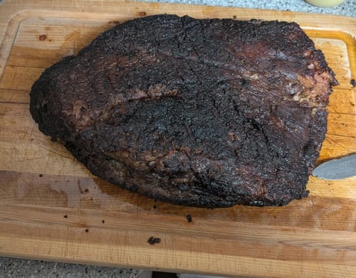 Customer's cooked USDA Prime Brisket with a dark crust resting on a wooden cutting board.